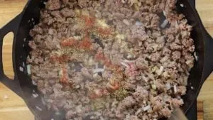 Ground beef and onions cooking in a cast iron skillet, seasoned with spices for a flavorful dish.