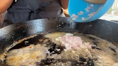 Diced shallots being added to sizzling butter in a black skillet for cooking.