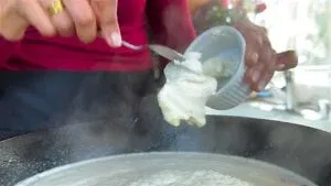 Person adding cream cheese to a steaming pan for cooking, close-up shot in a kitchen setting.