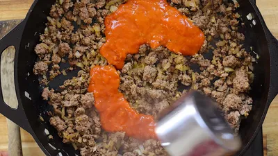 Cooking ground beef with tomato sauce in a skillet for a delicious meal preparation.