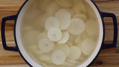 Sliced potatoes soaking in a pot of water on a wooden surface, ready for boiling.