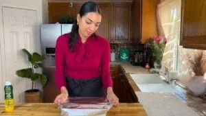 Woman in red shirt wrapping a dish with foil in a cozy kitchen setting.