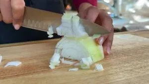 Cutting an onion on a wooden board with a sharp knife for a fresh cooking preparation.