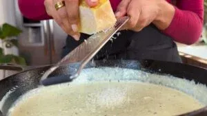 Grating cheese over creamy sauce in a skillet for a delicious homemade pasta dish.