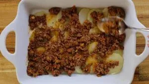 Layered potato casserole with seasoned ground meat in a white baking dish.