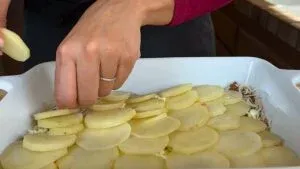 Person layering sliced potatoes in a baking dish for a potato casserole recipe.