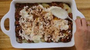 Preparing homemade moussaka: layering minced meat and sauce in a baking dish for a delicious Greek casserole.