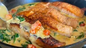 Pan-seared salmon in creamy sauce with tomatoes and spinach, cooked in a skillet.