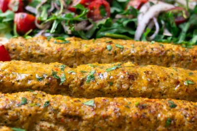 Grilled chicken kebabs with herbs and spices, served with fresh salad in the background.