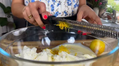 Grating lemon zest into cream cheese mixture in a glass bowl for a fresh dessert recipe.