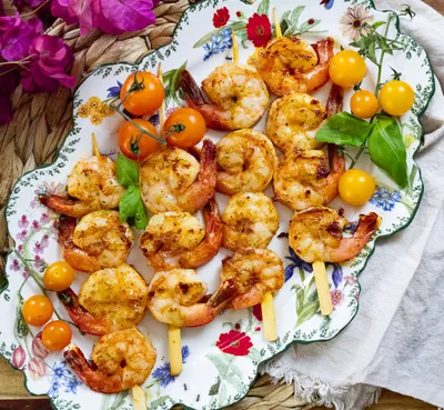 Grilled shrimp skewers with cherry tomatoes and basil on a floral plate.