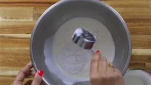 Mixing flour and cream in a steel bowl with a measuring cup on a wooden surface.