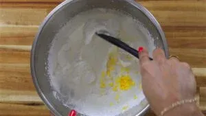Mixing lemon zest into whipped cream in a stainless steel bowl on a wooden surface.