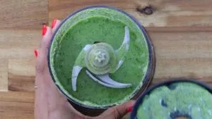 Blending vibrant pesto sauce in food processor on wooden table, close-up of refreshing homemade recipe.