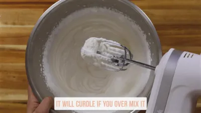 Electric mixer whipping cream in a bowl with a note saying, It will curdle if you over mix it.