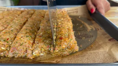 Cutting homemade vegetable-packed meat slices with a sharp knife on a parchment-lined baking tray.