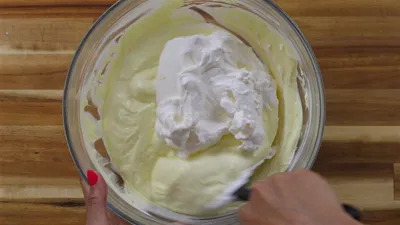 Creamy batter being mixed in a glass bowl on a wooden surface.