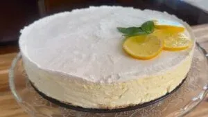 Cheesecake topped with lemon slices and mint on a glass stand, perfect for dessert lovers.