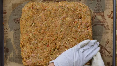 Gloved hand shaping seasoned minced chicken mixture on parchment paper.