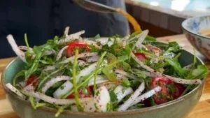 Fresh salad with tomatoes and onions being dressed with sauce in a green bowl.