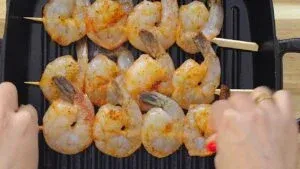 Grilled shrimp skewers being cooked on a grill pan, seasoned with spices.