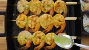 Grilled shrimp skewers on a pan, drizzled with basil sauce. Perfect for seafood lovers and summer grilling.
