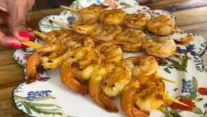 Grilled shrimp skewers on a floral plate, beautifully seasoned and ready to serve as a delicious seafood dish.