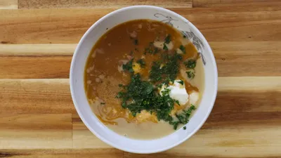 Bowl of tahini sauce topped with fresh herbs on a wooden table.