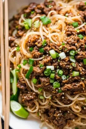 Delicious Asian noodles with seasoned beef, scallions, and sesame seeds, served in a white bowl with chopsticks.