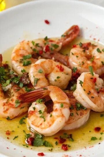 Juicy shrimp in garlic butter sauce garnished with parsley and red pepper flakes on a white plate.