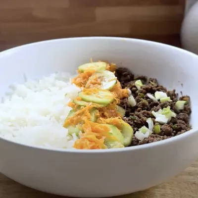 Rice bowl with ground beef, shredded carrots, and green onions in a white bowl. Perfect healthy meal option.