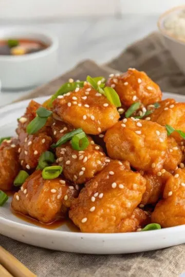 healthy orange chicken topped with sesame seeds and green onions, served with rice and sauce.