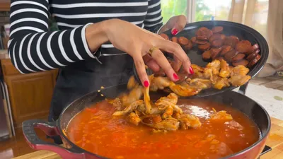 Person adding sausage and chicken to a simmering risotto in a kitchen.