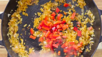 Diced onions and red peppers sautéing in a black skillet for a savory dish.
