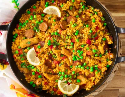 A vibrant pan of chicken and chorizo risotto with peas, and lemon slices on a wooden table.