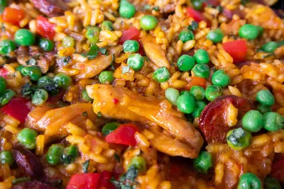 Close-up of flavorful chicken paella with peas, bell peppers, and chorizo, showcasing vibrant ingredients.
