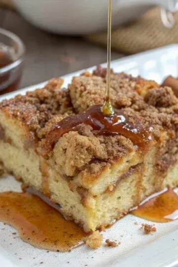 Close-up of cinnamon coffee cake drizzled with honey on a white plate, garnished with cinnamon sticks.