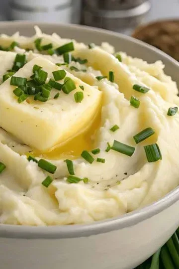 Creamy mashed potatoes topped with melting butter and fresh chives in a white bowl.