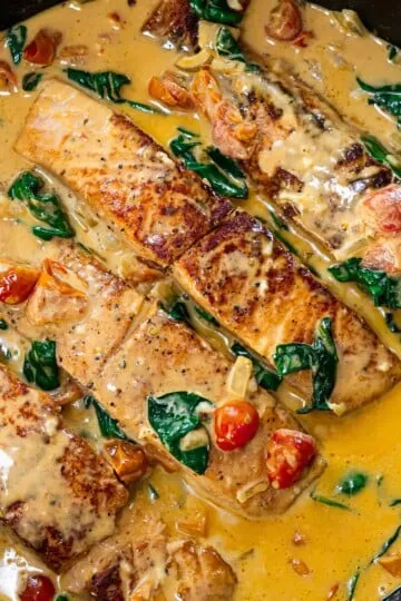Pan-seared salmon in creamy sauce with cherry tomatoes and spinach. Perfect for a gourmet meal.