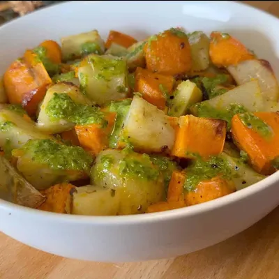 Roasted sweet potatoes and root vegetables with green herb sauce in a white bowl.