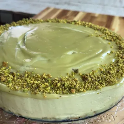 Creamy no bake pistachio cheesecake with a smooth green frosting and crushed pistachio topping on a wooden board.