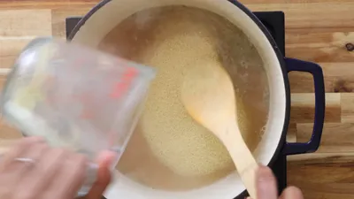 Cooking couscous with broth in a pot, stirred with a wooden spoon.