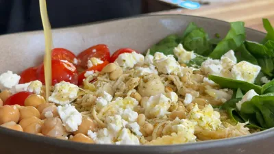 Fresh salad with chickpeas, feta, cherry tomatoes, spinach, and dressing being poured.