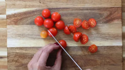 Slicing fresh cherry tomatoes on a wooden cutting board with a knife.