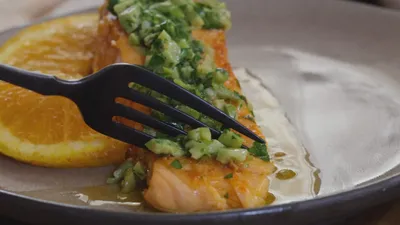 Grilled salmon with avocado salsa and orange slice on a plate with fork.