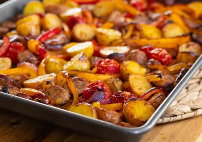 Sheet pan with roasted potatoes, sausage, and colorful bell peppers.