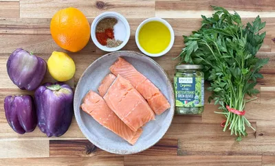 Fresh salmon, herbs, and vegetables arranged on wooden surface for a healthy cooking recipe.