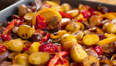 Sheet pan with roasted sausage, potatoes, and colorful bell peppers.