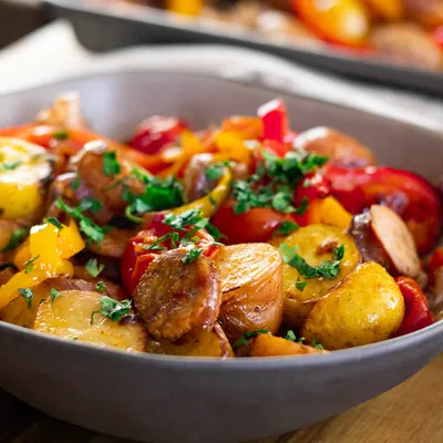 Delicious roasted sausage, peppers, and potatoes and herbs in a serving dish.