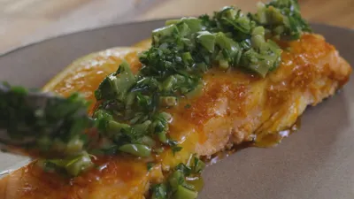 Grilled salmon fillet topped with fresh herbs and olives on a plate.